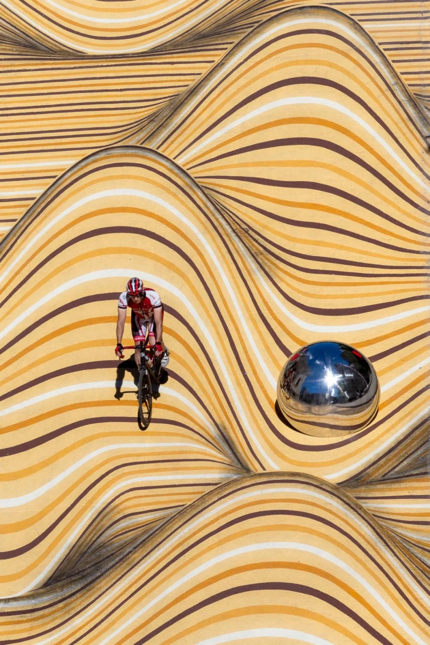 Pedestrian walking across rippling painted bands that seem to rise from the ground
