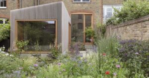 this-home-extension-covered-in-vertical-wood-slats-includes-a-picture-window-overlooking-the-garden