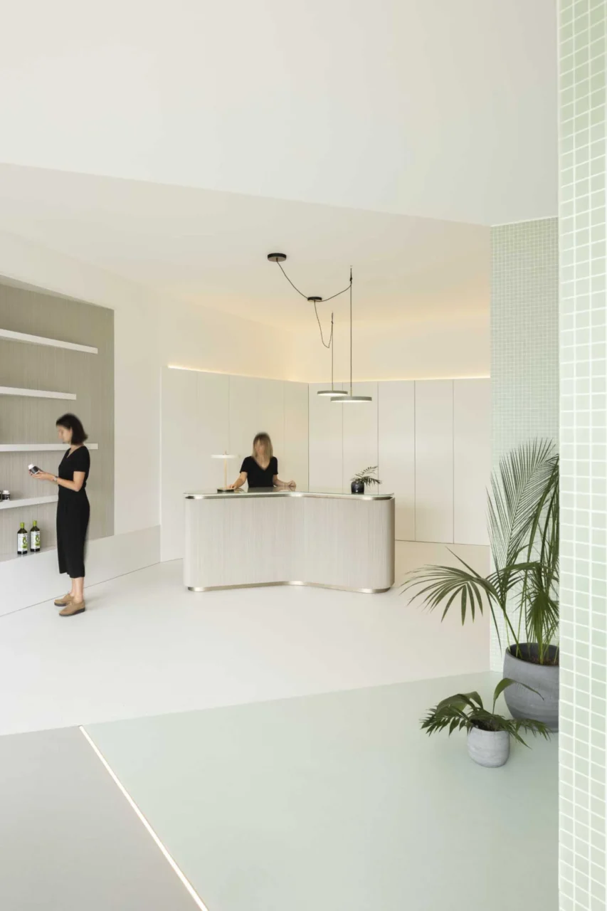 Reception with a curved desk and wall shelf, next to the pastel green waiting area