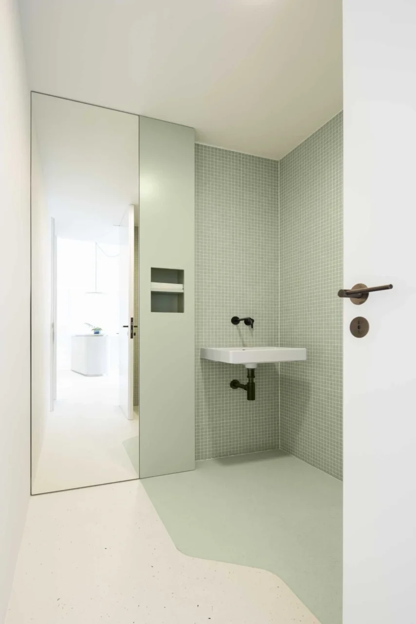 Clinic bathroom with pastel green wall tiles behind a white door