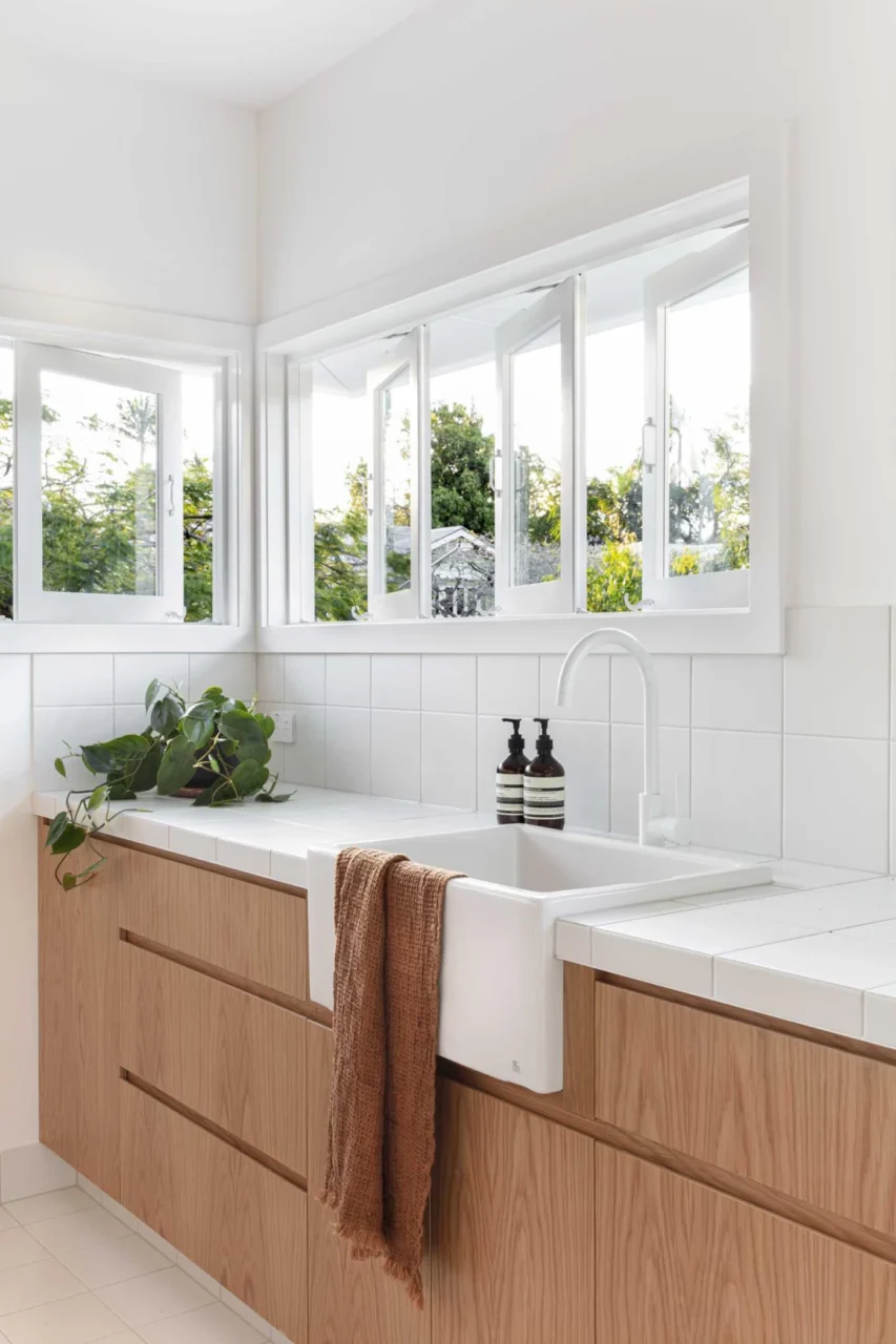 Laundry with hardware-free wood cabinets, a white apron sink and white tiled countertop