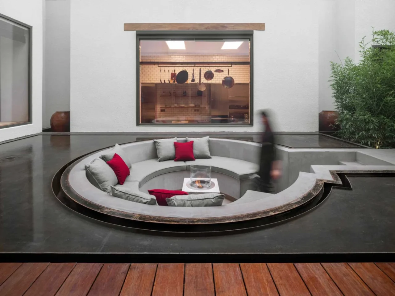 Round sunken conversation pit with grey built-in seating and red cushions, set in shallow water at a Beijing house
