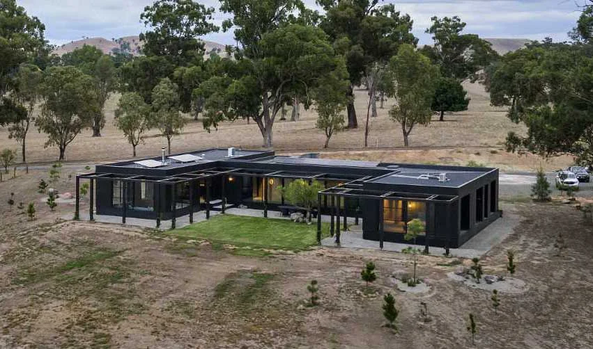 U-shaped rural house with a black exterior and timber accents by Dion Keech Architects