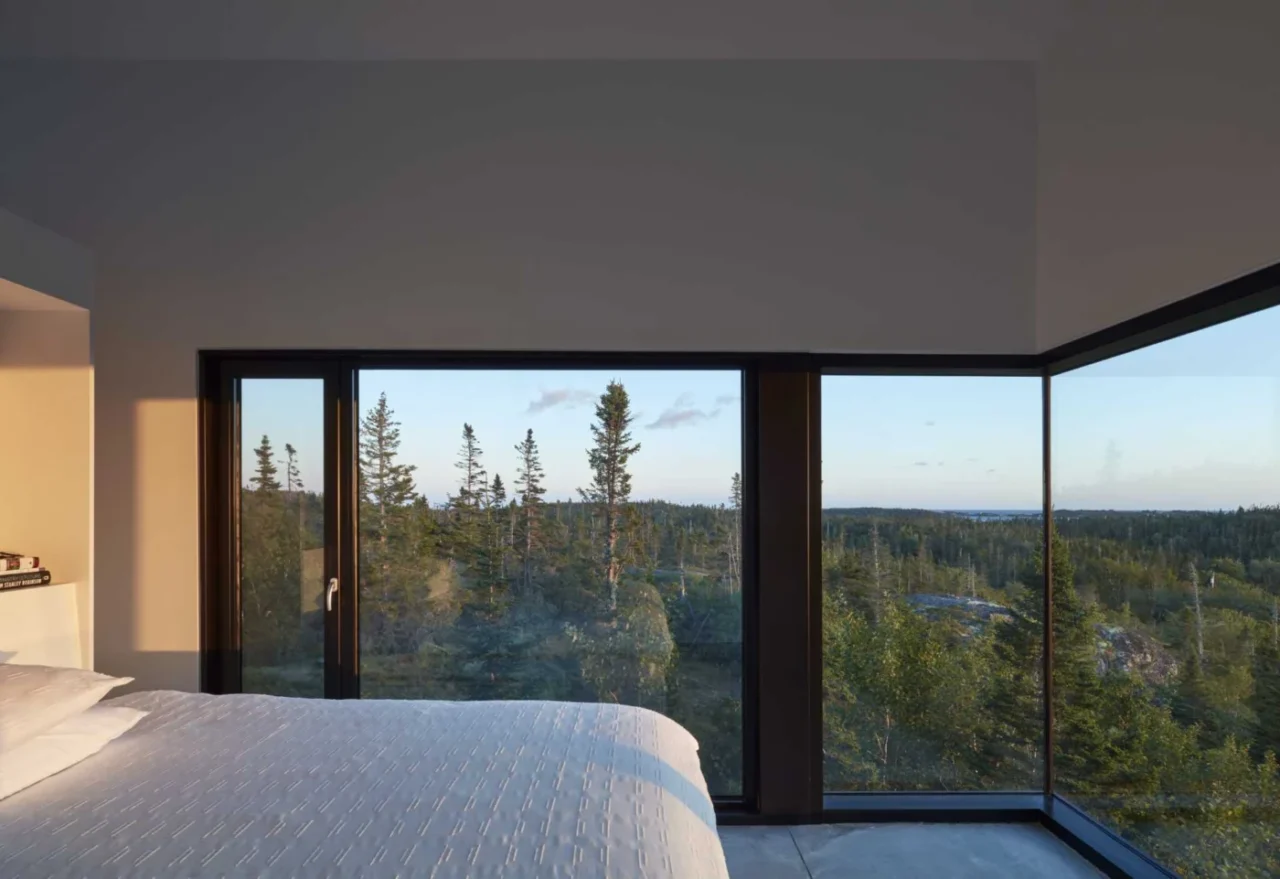 Bedroom with wrap-around black-framed windows facing the trees