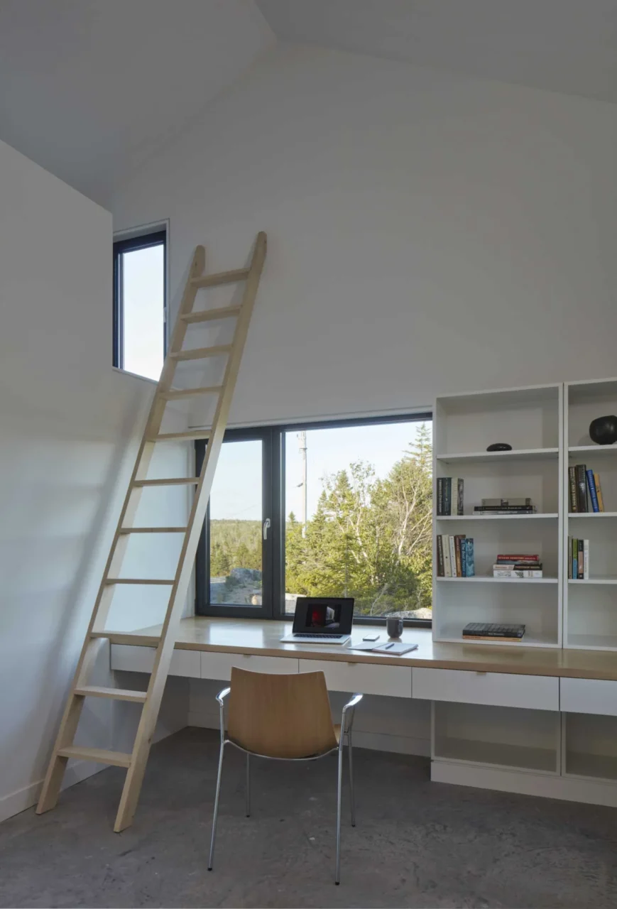 Room with a built-in desk and a ladder up to a loft