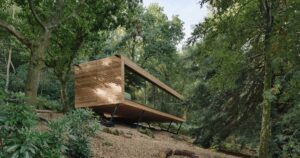 this-wood-covered-house-hovers-above-the-hillside-in-the-forest