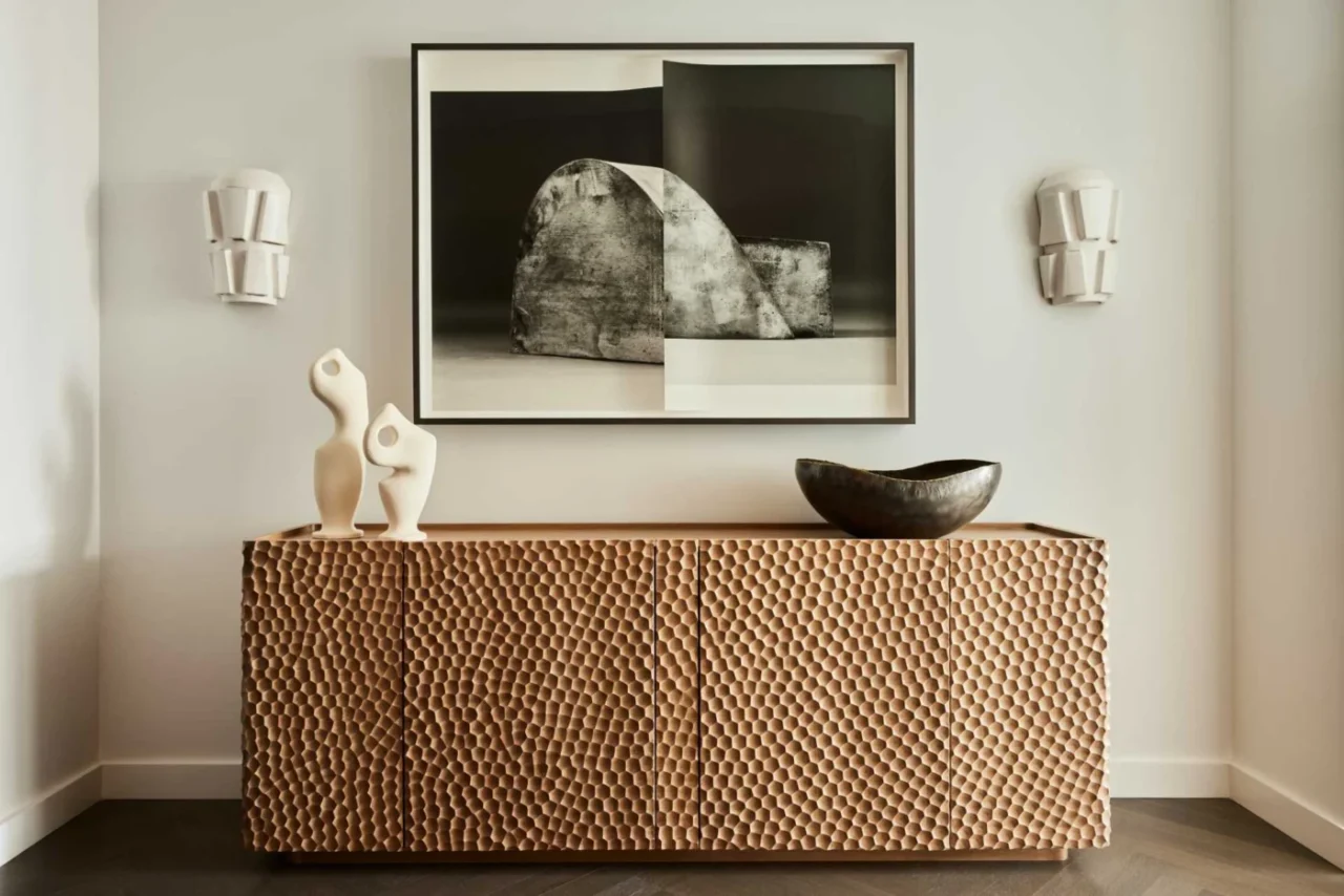 Gouged wood credenza in the foyer with art and ceramic sconces above