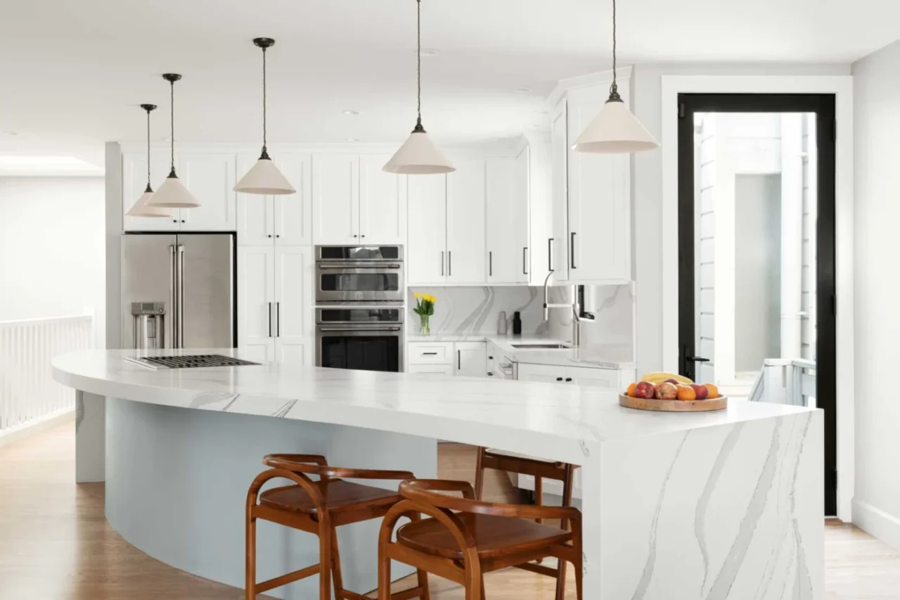 Serpentine kitchen island with coloured lower cabinets and a range with a telescoping downdraft hood