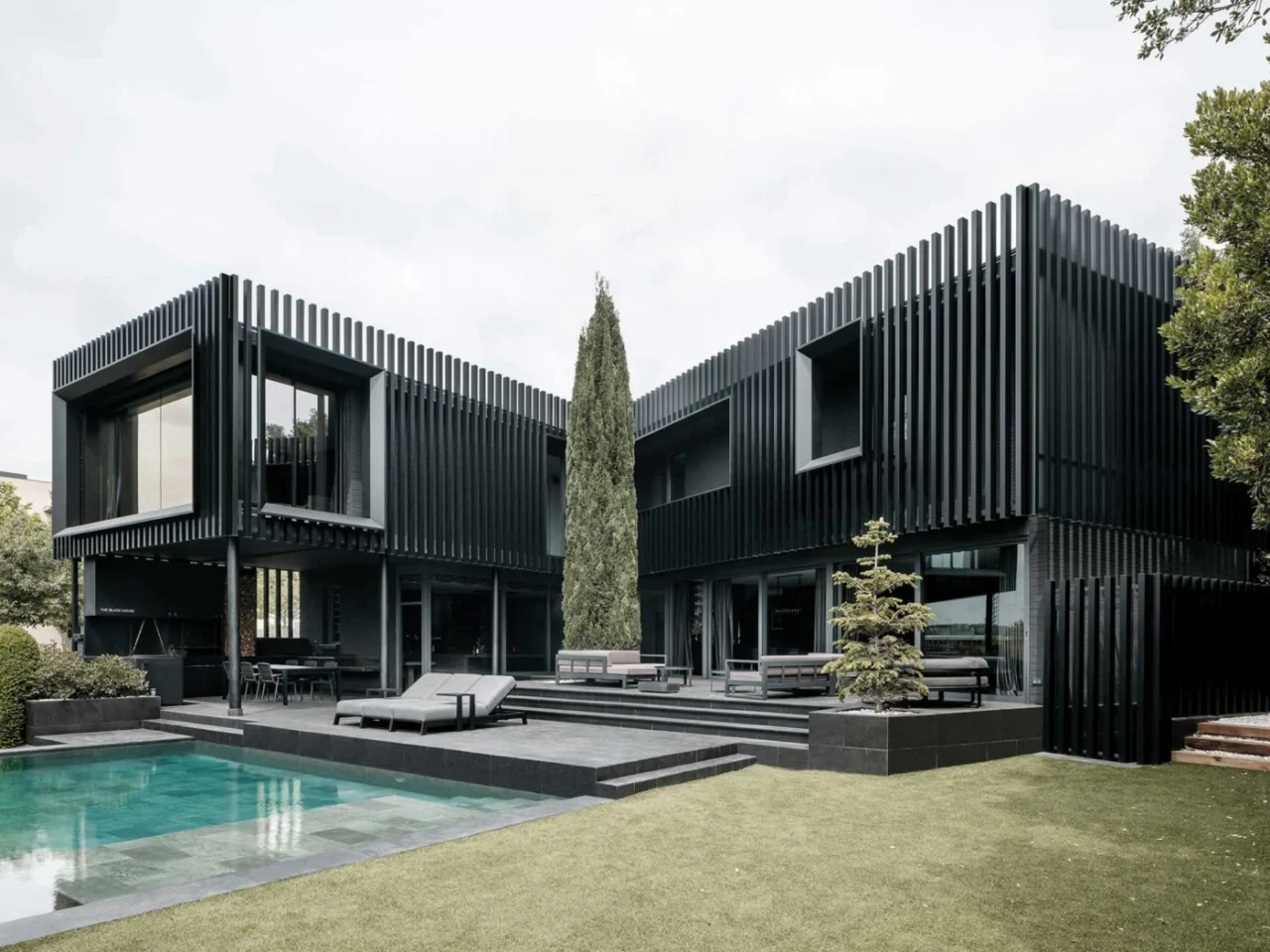 Black remodelled house by MDAMMM wrapped in vertical fins, seen from the garden and pool