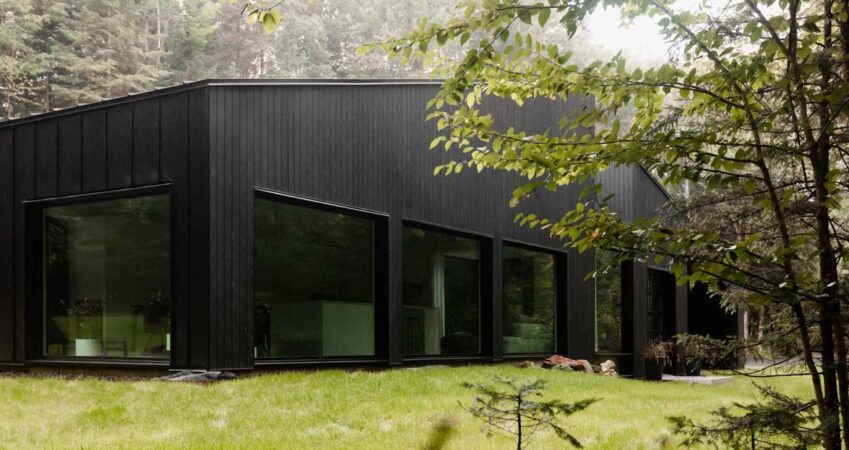 the-black-exterior-of-this-home-in-the-forest-covers-a-white-minimalist-interior