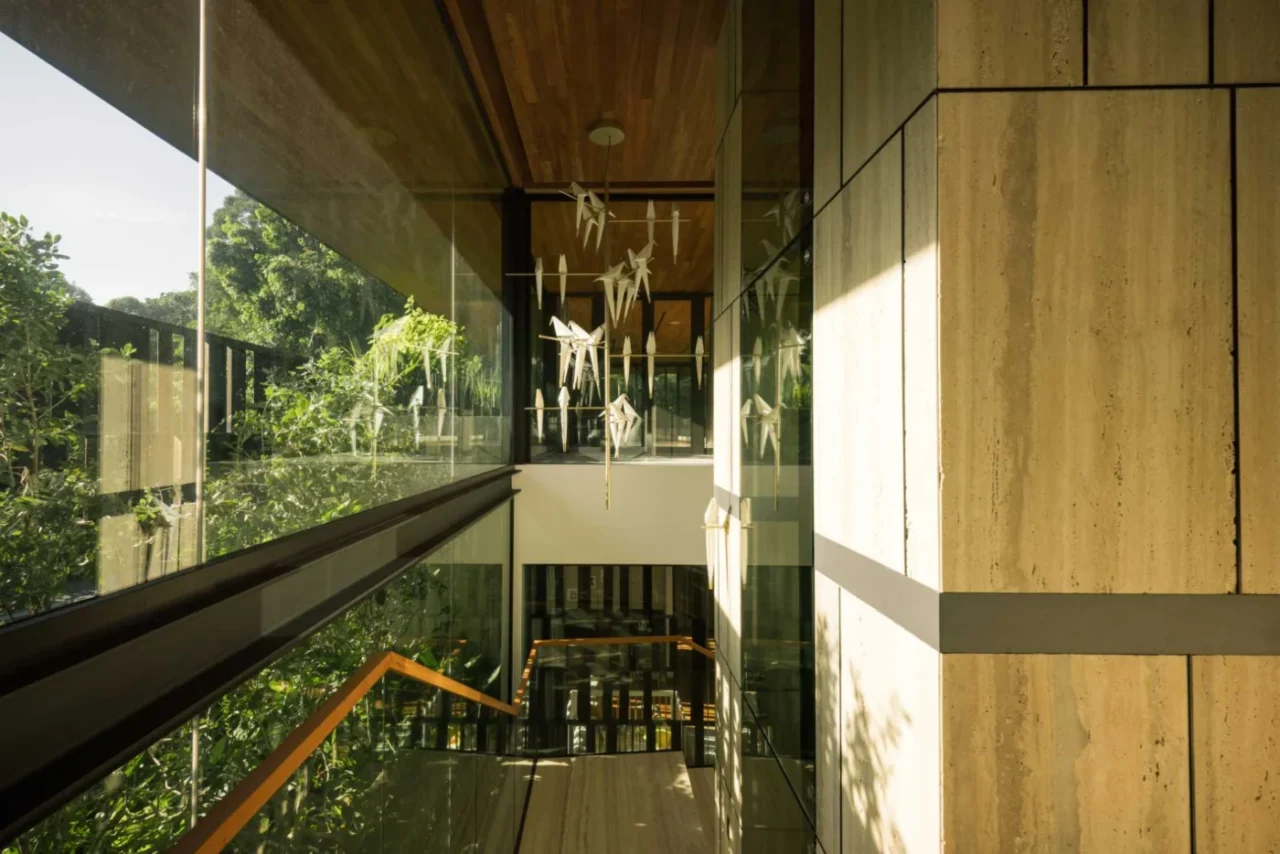 Tall wall of windows running alongside the stairs, with screens and vines outside