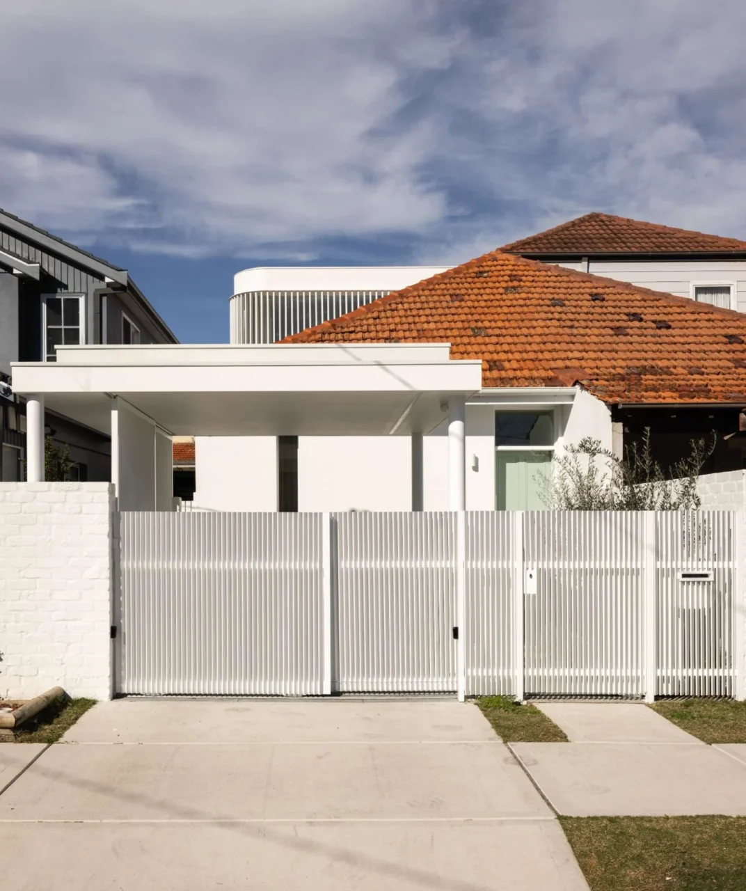 After: white front facade with a carport, vertical white screening and soft landscaping under the original red tiled roof