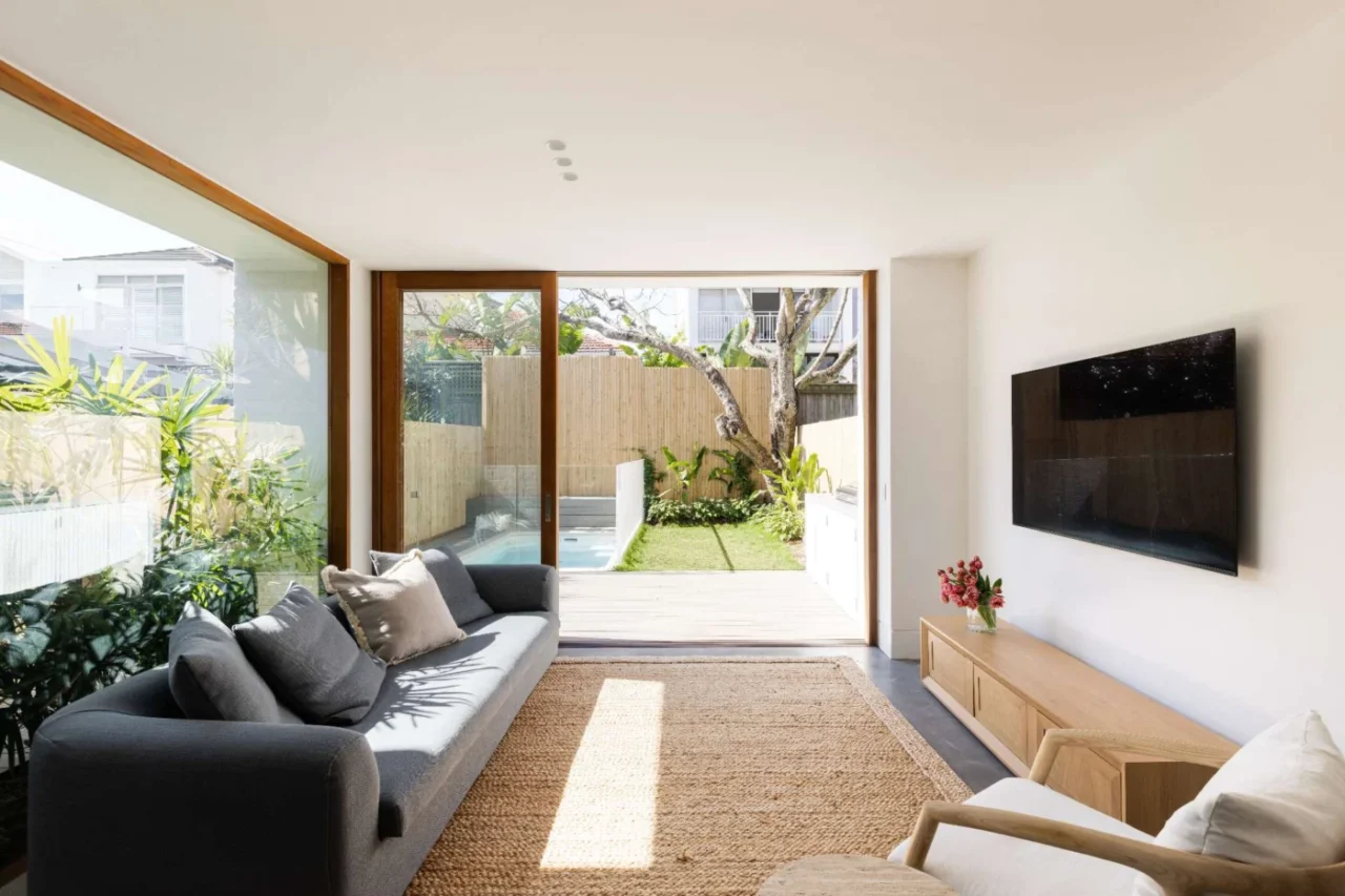 After: open-plan living room with floor-to-ceiling glass doors, a low grey sofa and a jute rug