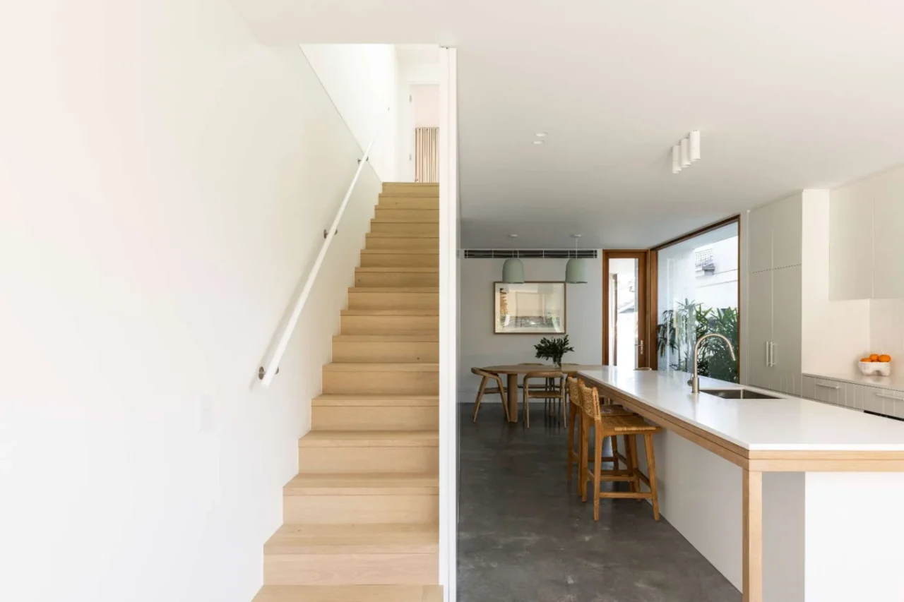 After: minimalist kitchen with matte white cabinetry, a long wood-accented island and woven stools
