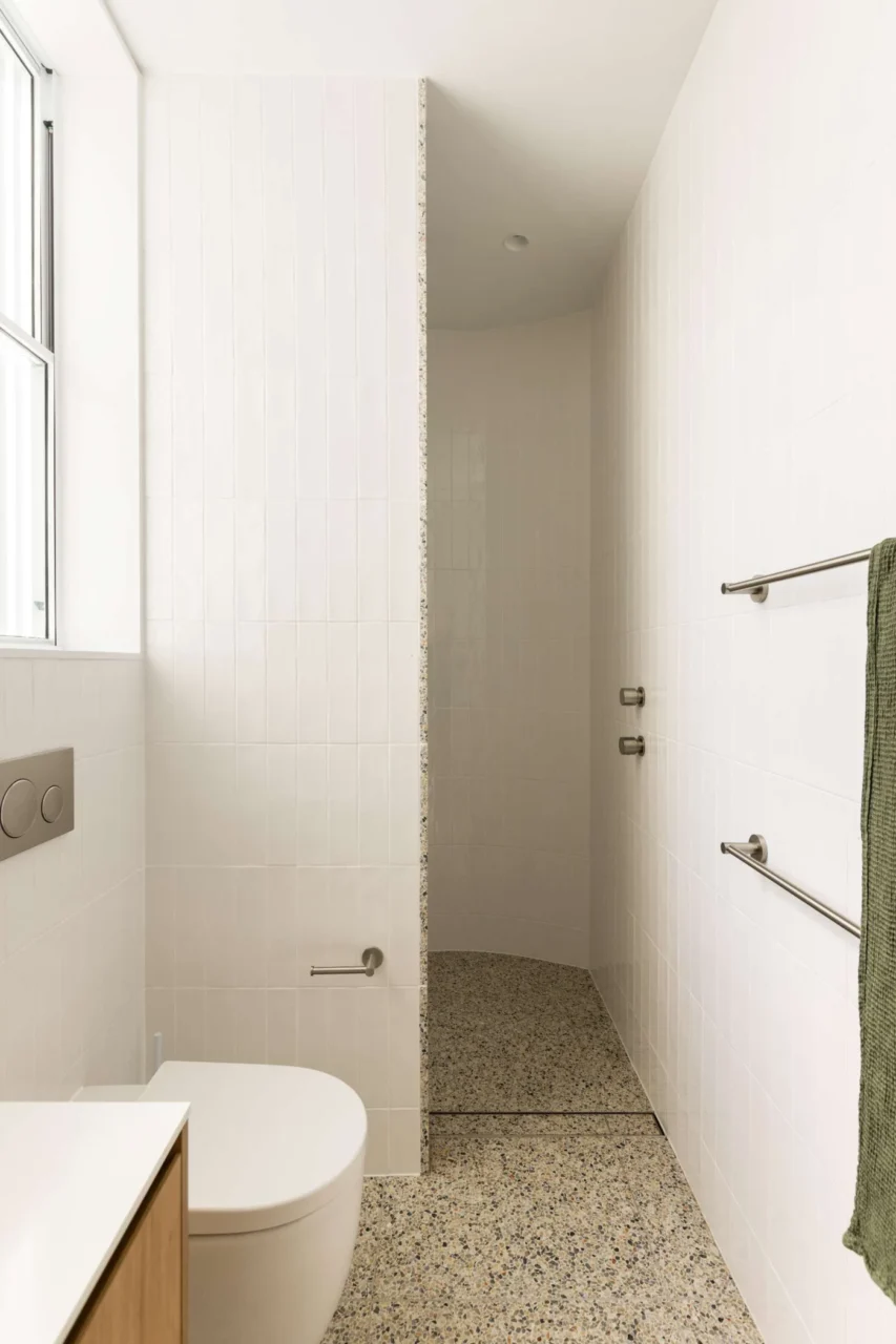 After: main ensuite with a curved shower wall, off-white tiles and terrazzo floor