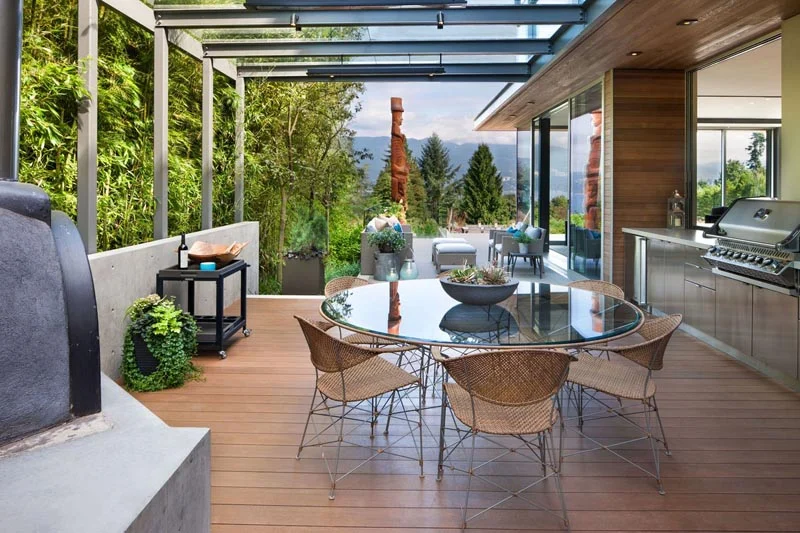 Outdoor dining area with a glass-topped table and built-in BBQ by Garret Cord Werner