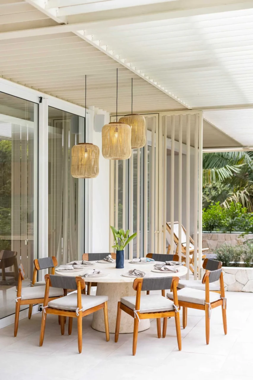 Round outdoor dining table with wood chairs among plants, Studio Saxe