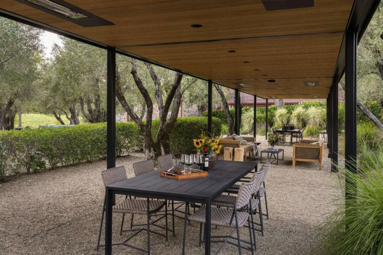 Outdoor dining area under a wood-lined pergola with black steel framing and woven chairs
