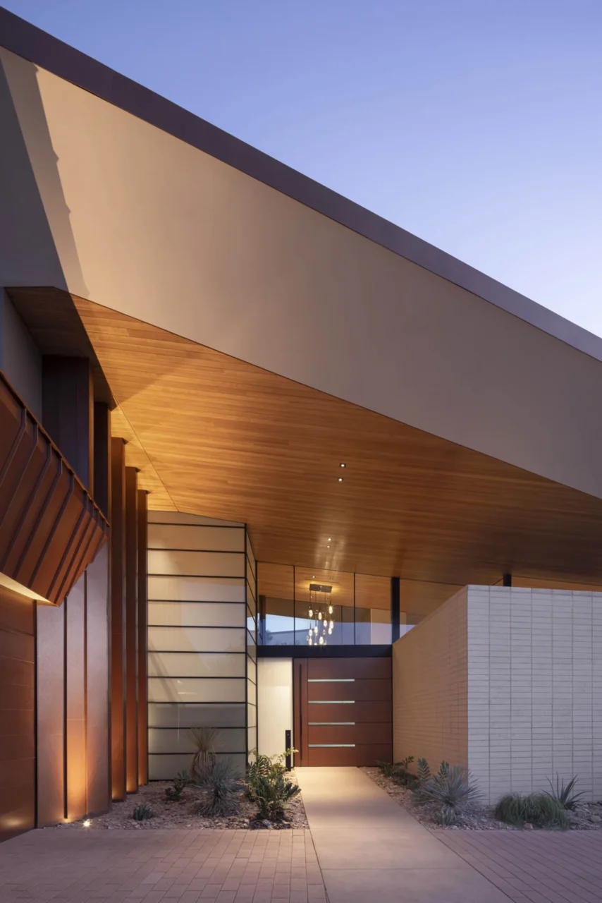 Large pivot entrance door in weathered metal panels framed in black steel